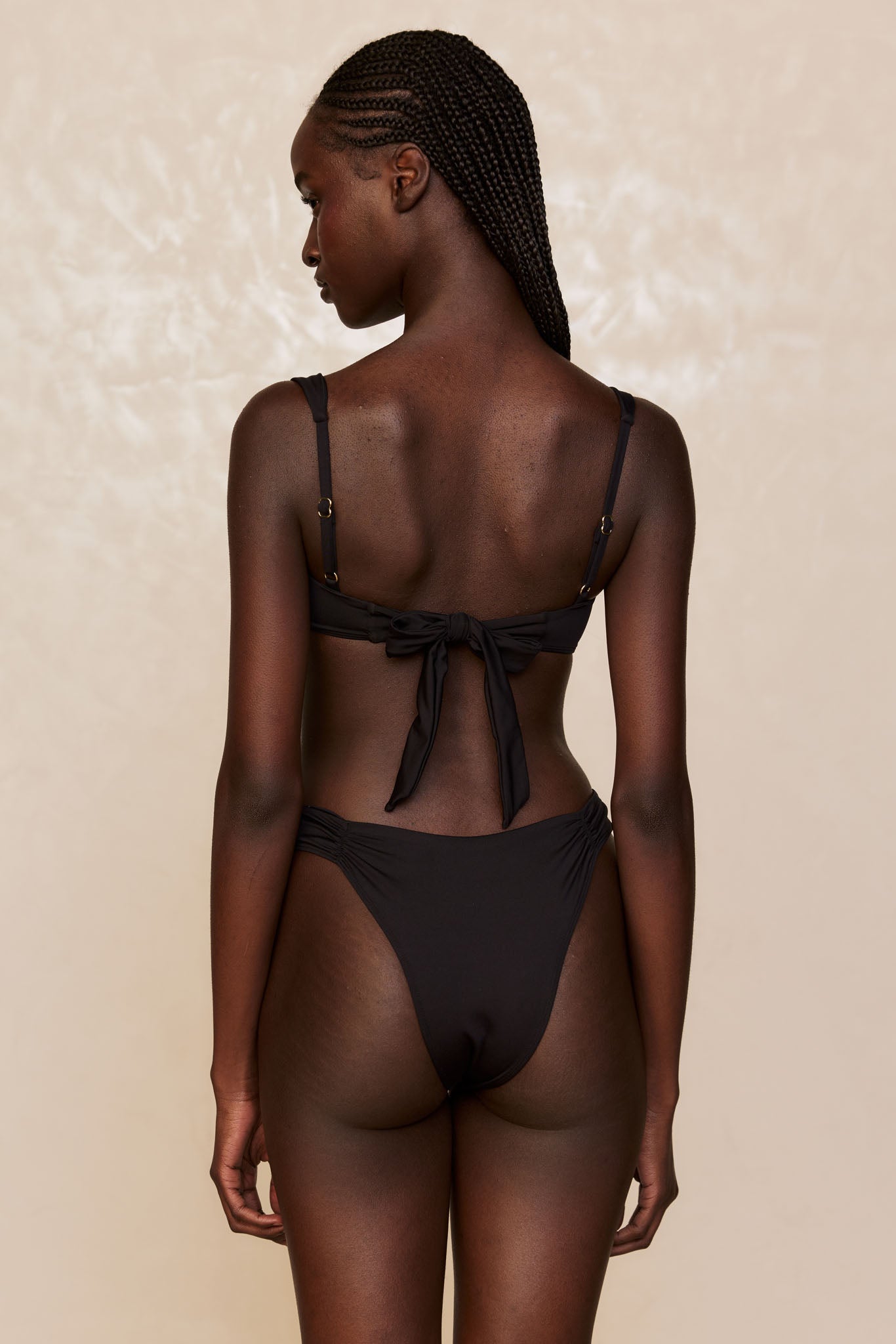 Rear view of a woman modeling a black bikini with braided hair and a tied bow at the back.