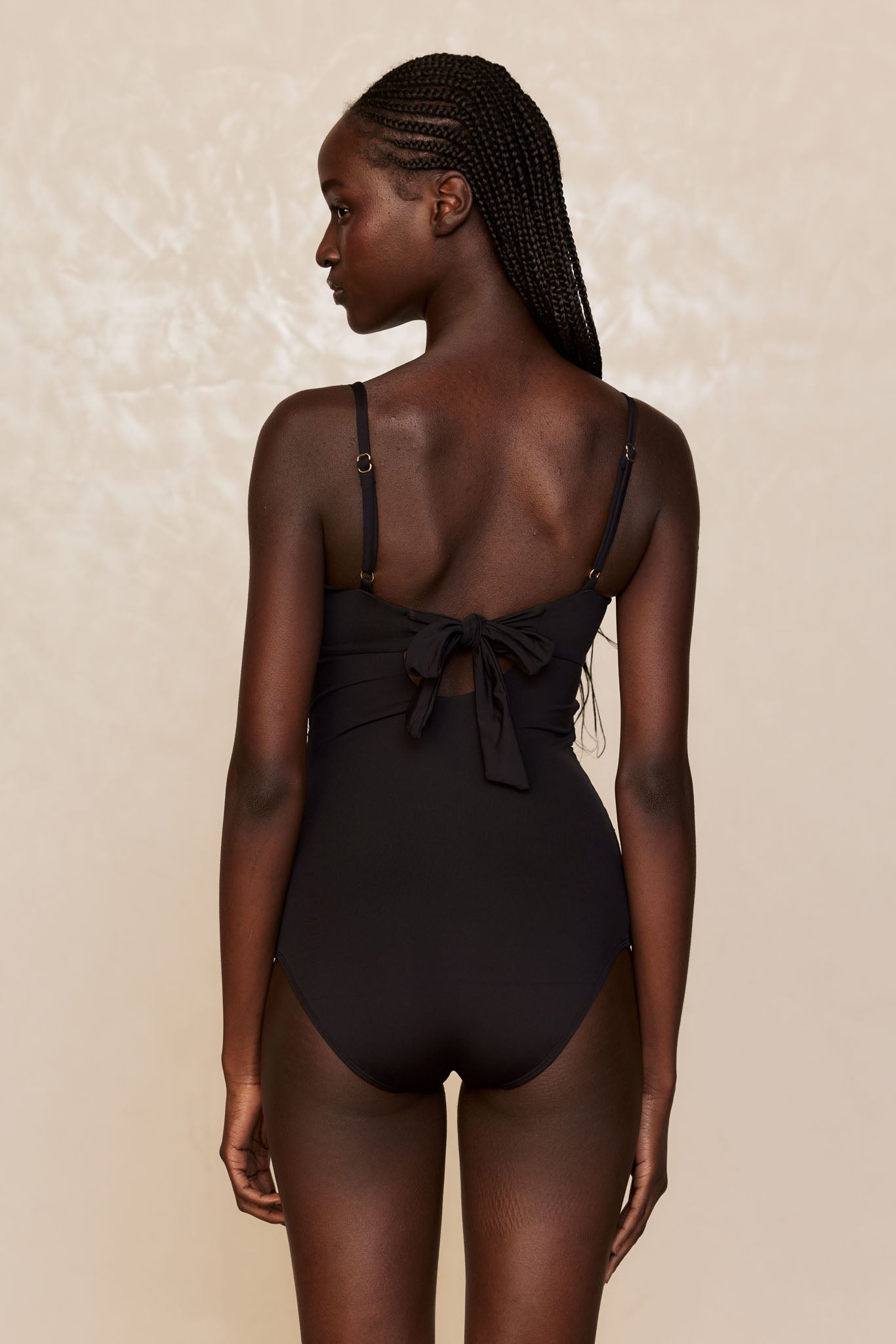 Rear view of woman in black one-piece swimsuit with a tied bow at mid back