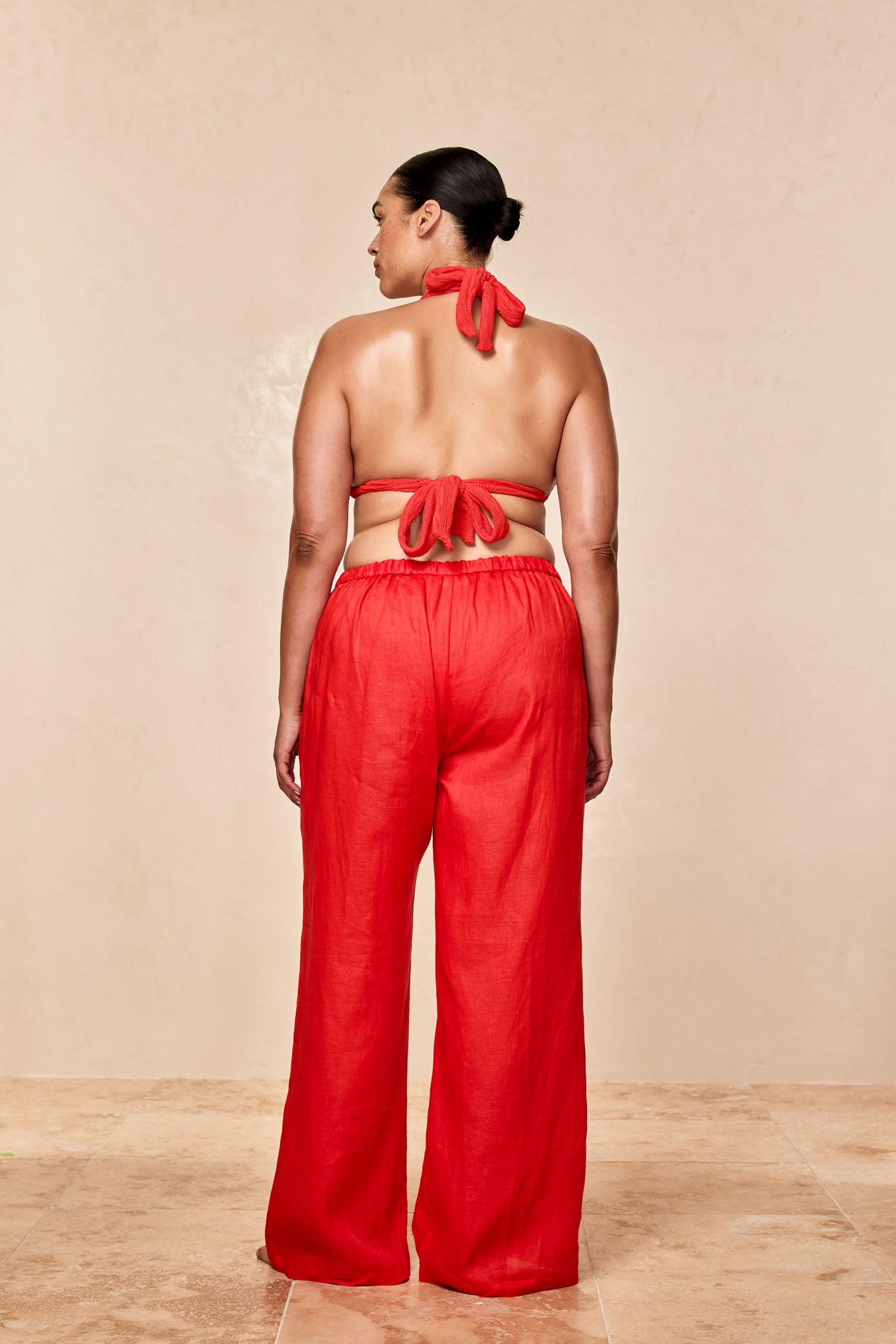 Back view of woman wearing a red halter top tied at neck and back and matching wide-leg red pants against a beige backdrop