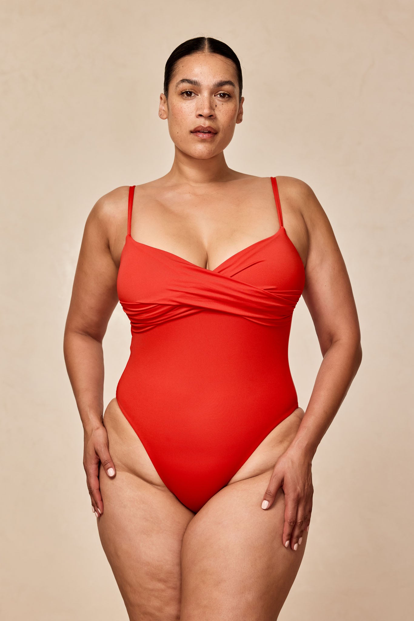 Front view of person in a red one-piece swimsuit against a neutral beige background.
