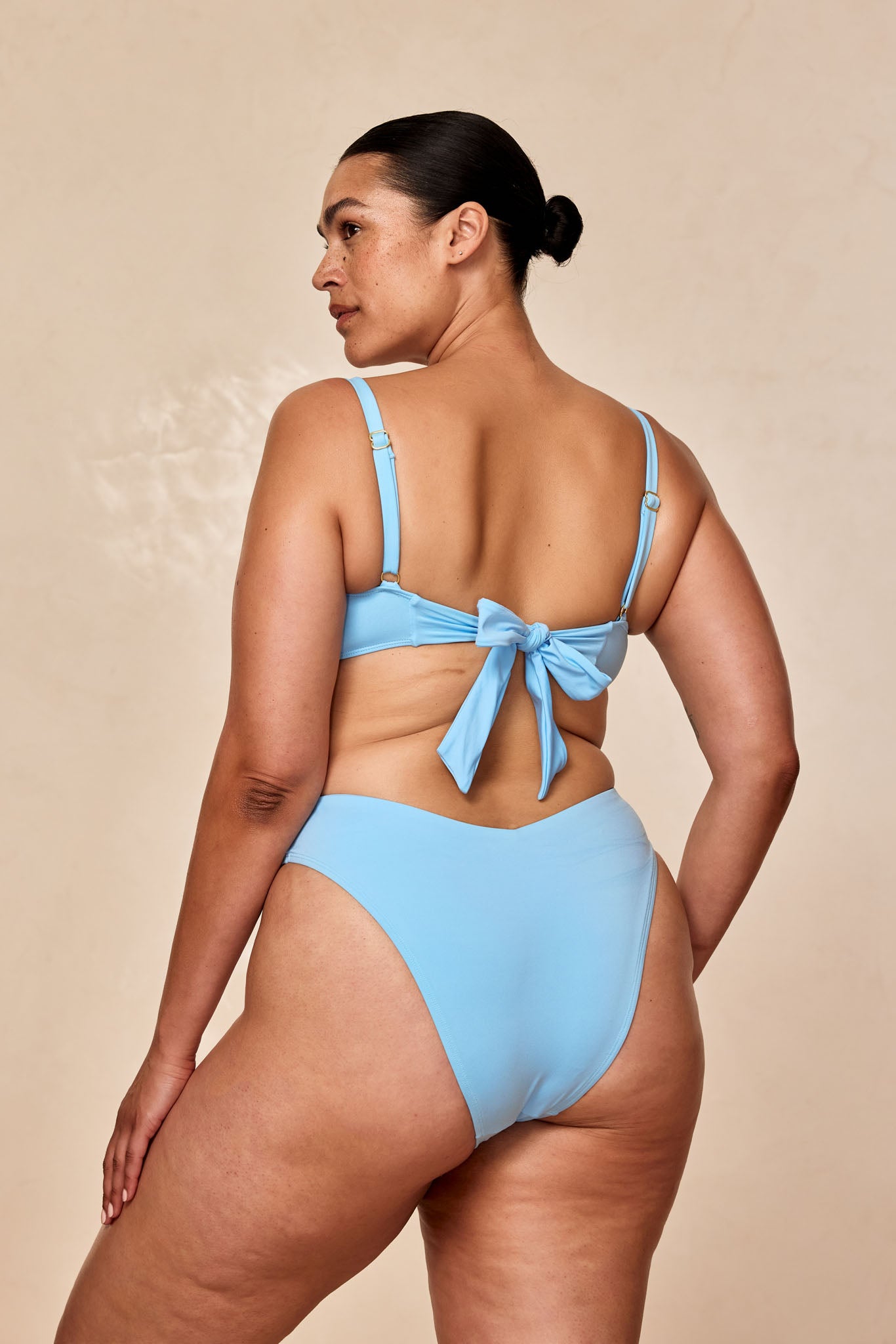 Back view of a plus-size woman wearing a light blue bikini with a tied bow at the center back.