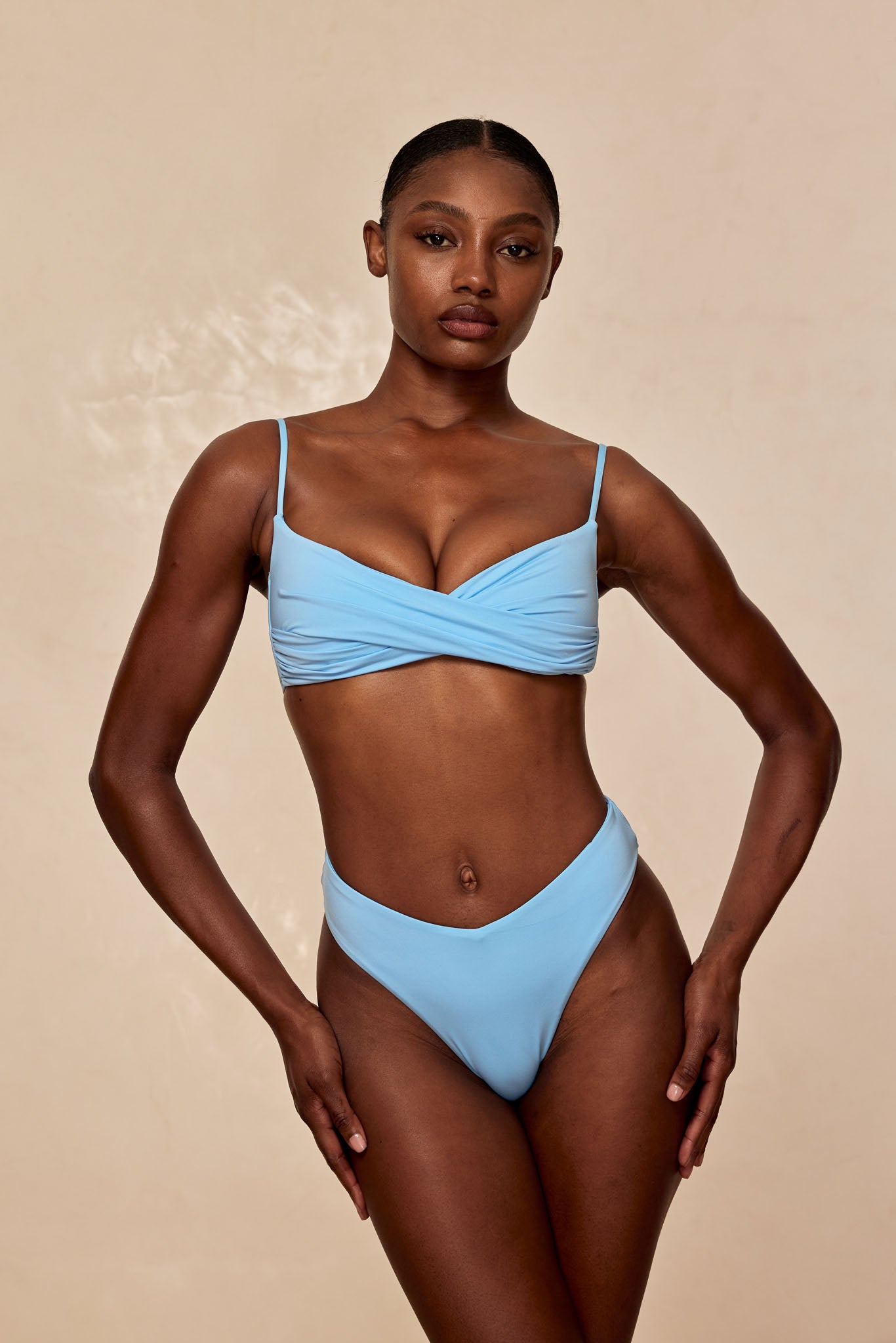 Model standing front-facing wearing a light-blue bikini against a plain beige background.
