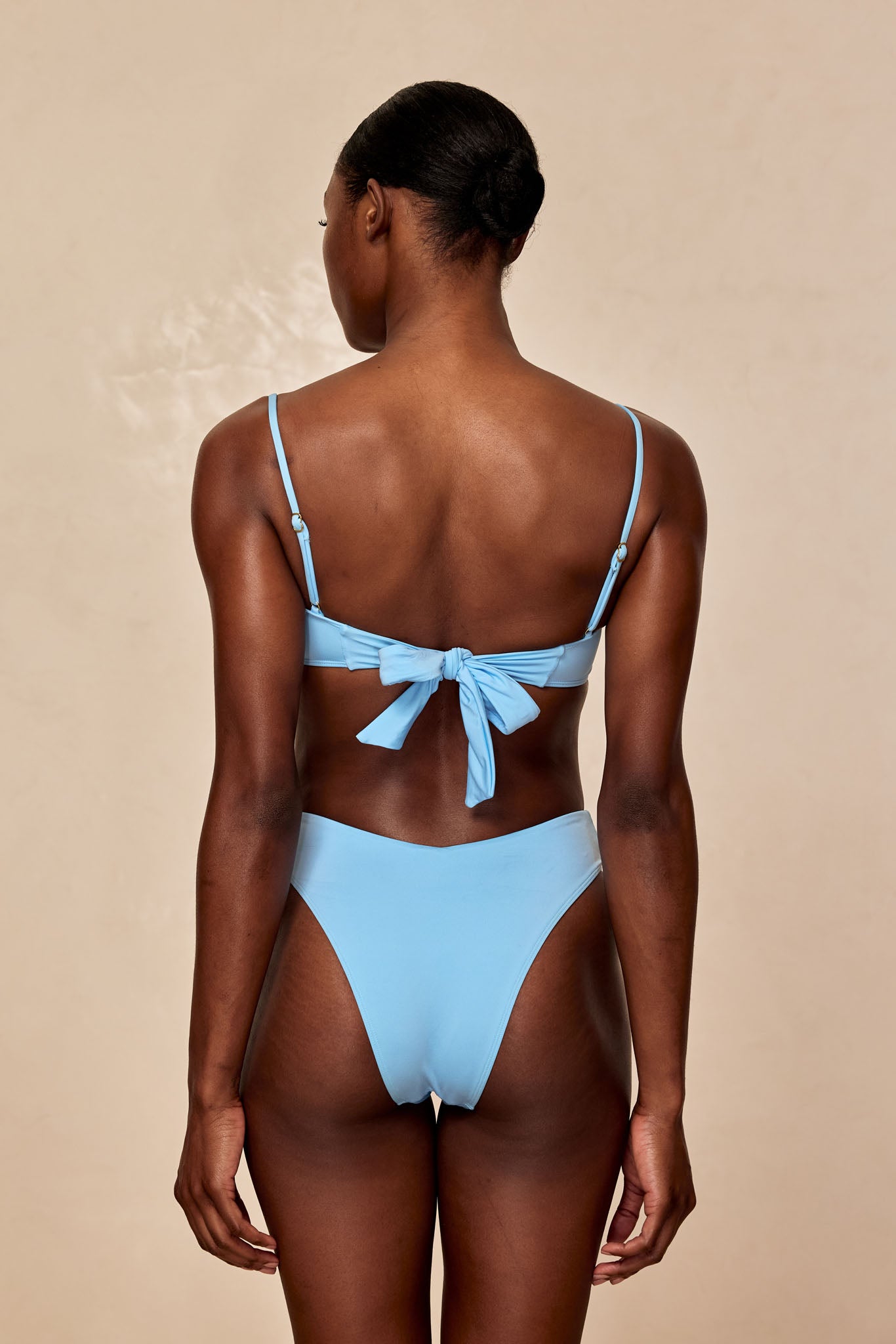 Rear view of a person wearing a light-blue tie-back bikini top and high-cut bikini bottoms.