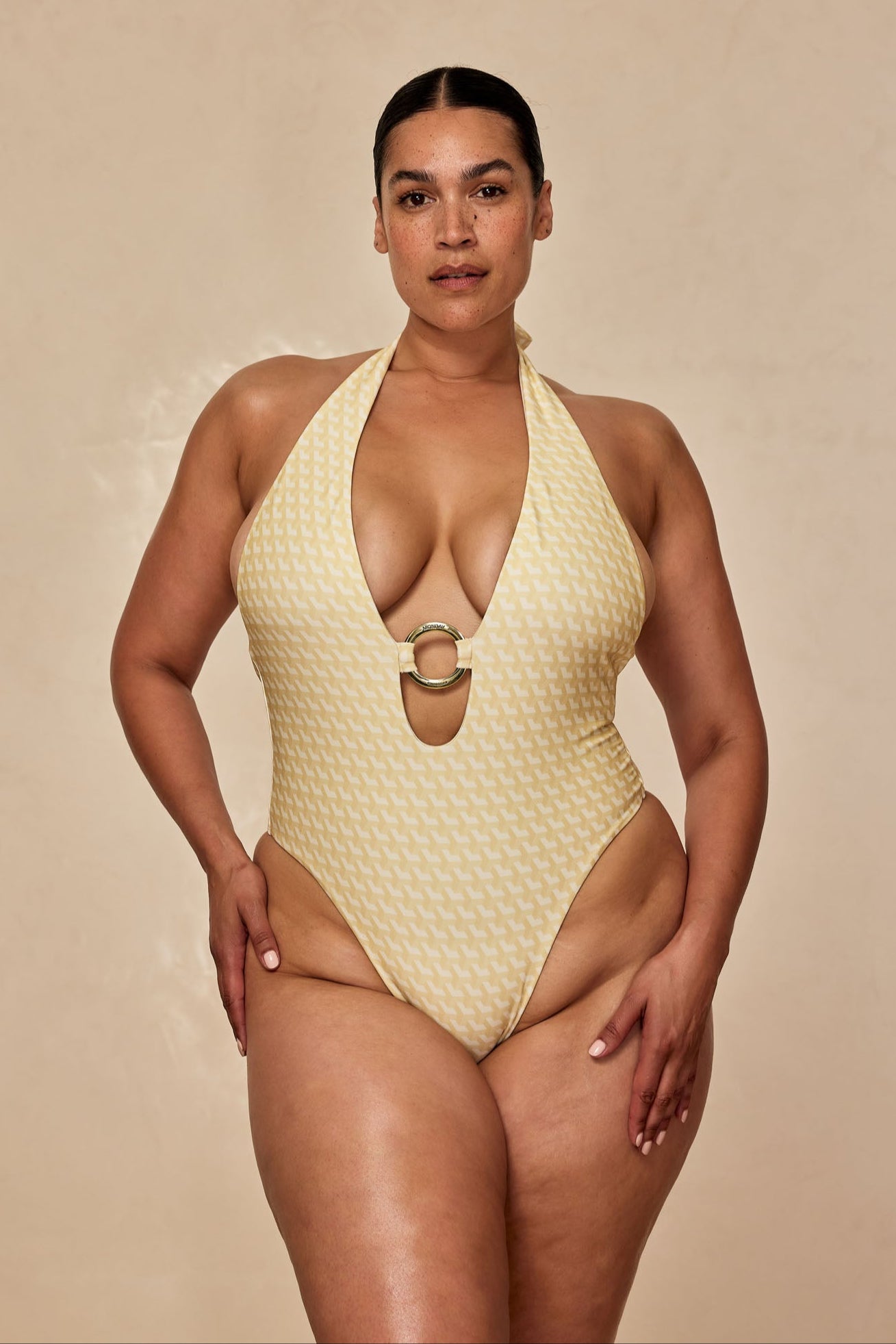 Woman wearing yellow patterned halter one-piece swimsuit with plunge neckline and decorative ring at center