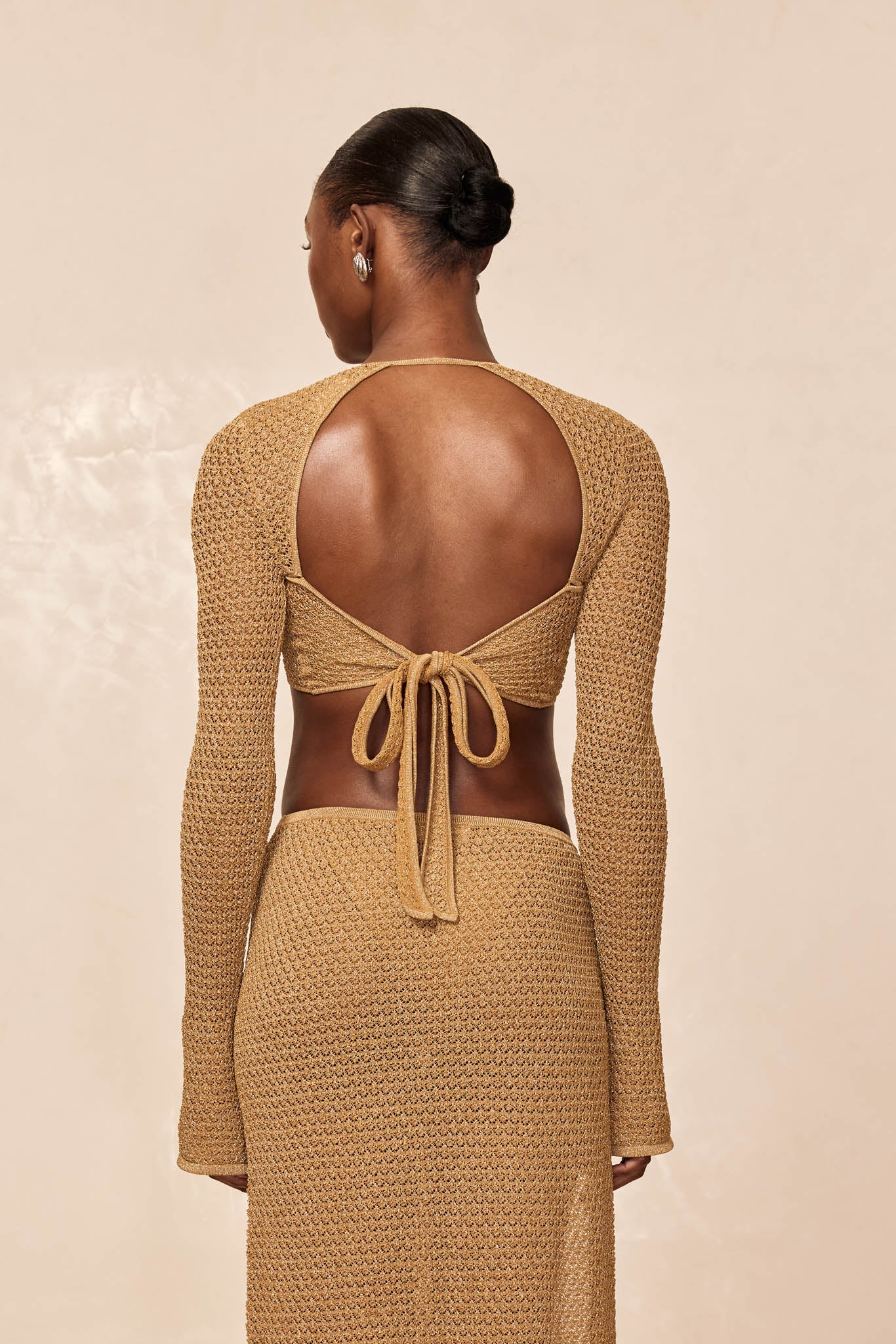 Model from back wearing tan crocheted open-back tie-top tied in bow and matching skirt.