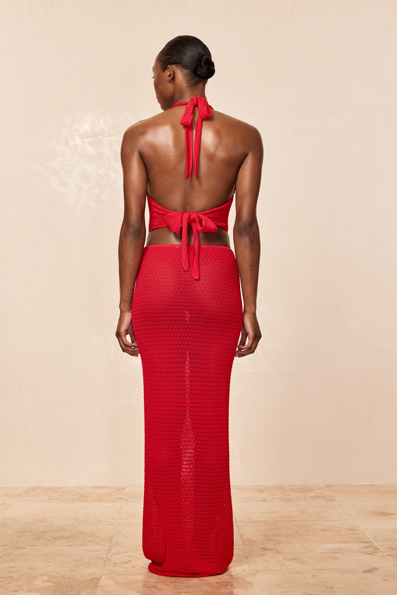 Woman seen from back wearing a red crochet halter top tied at the back with a matching long crochet skirt.
