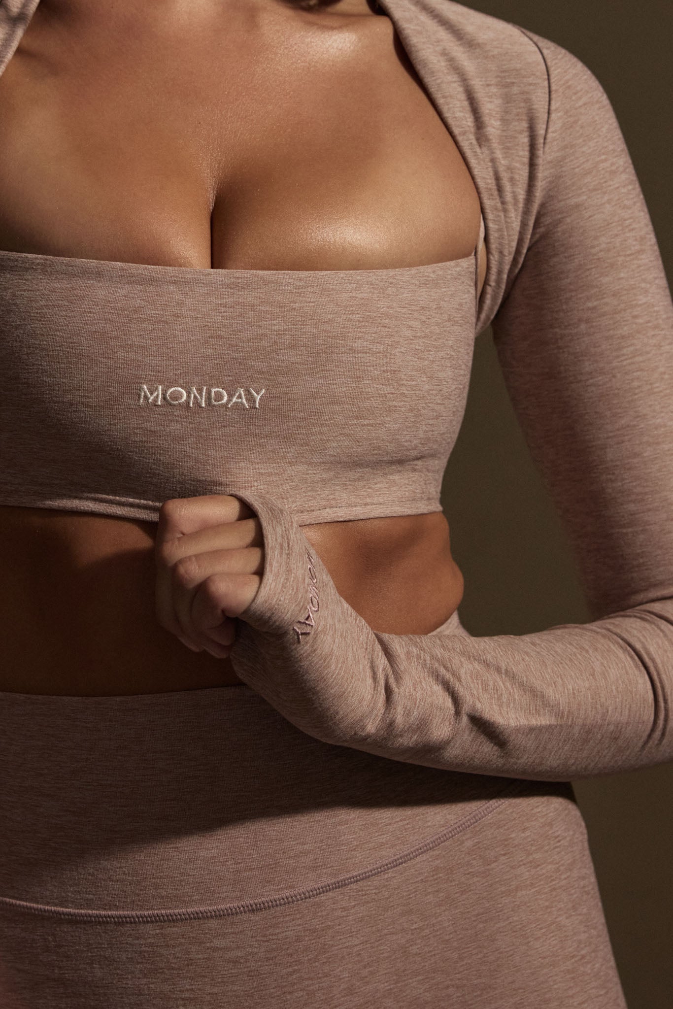 Torso wearing mauve seamless activewear; 'MONDAY' embroidered on bandeau, hand pulling thumb-loop on long sleeve.