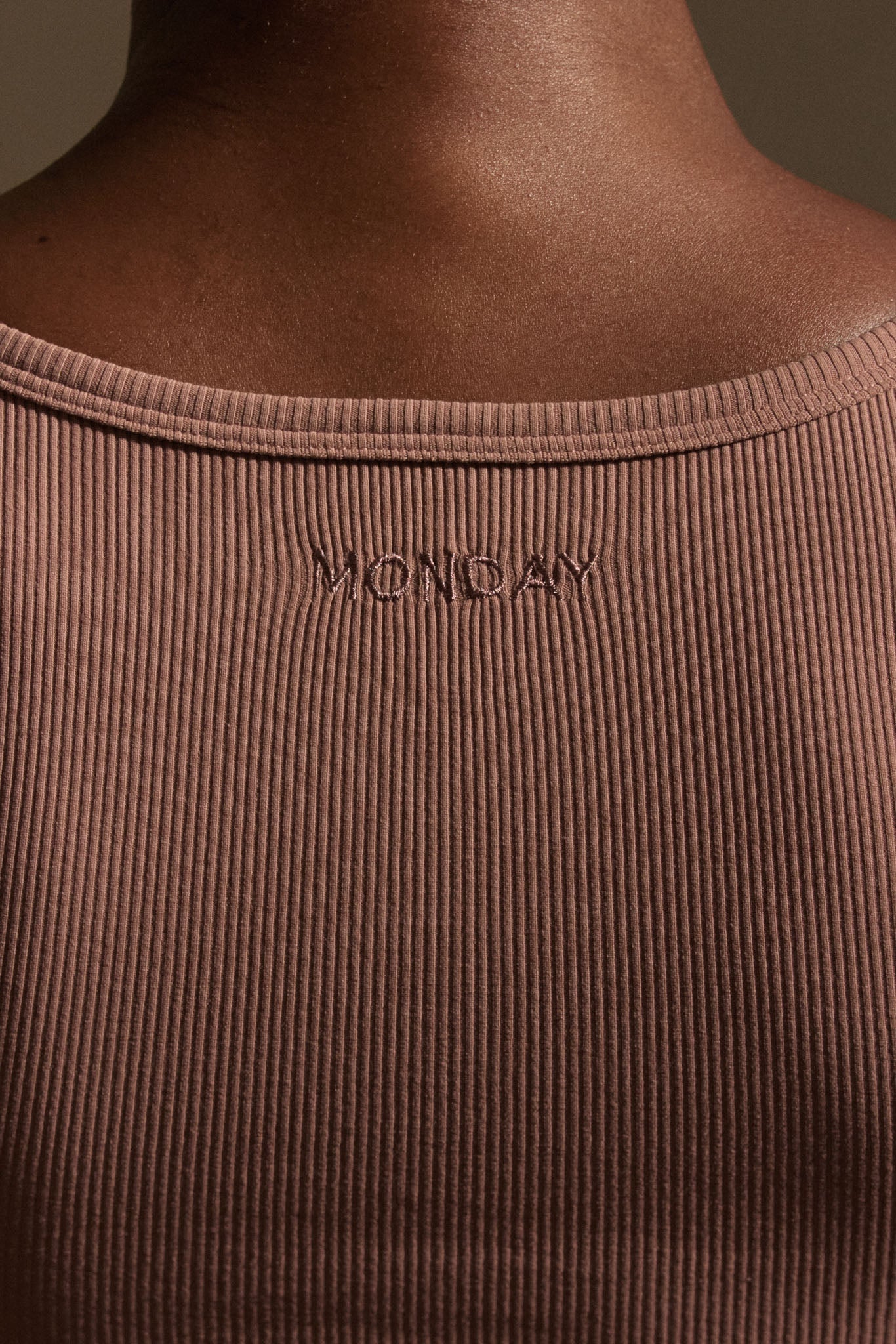 Ribbed mauve tank back with embroidered MONDAY below the neckline on person's upper back.
