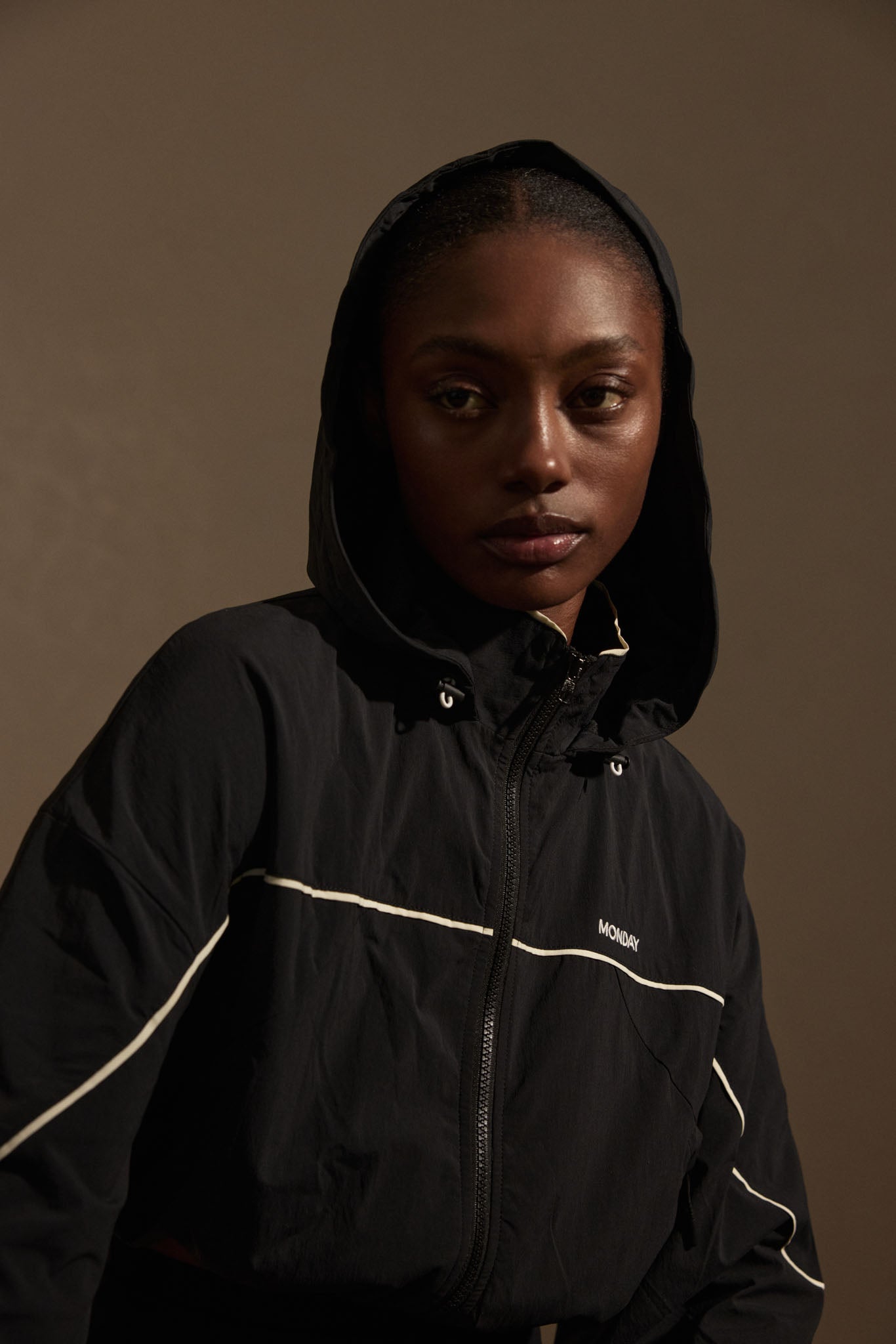 Woman wearing black hooded jacket with white piping; 'MONDAY' logo on chest.