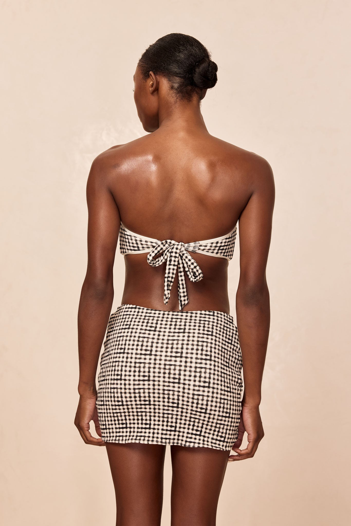 Rear view of person wearing black-and-white gingham bandeau top tied in a bow with matching mini skirt.