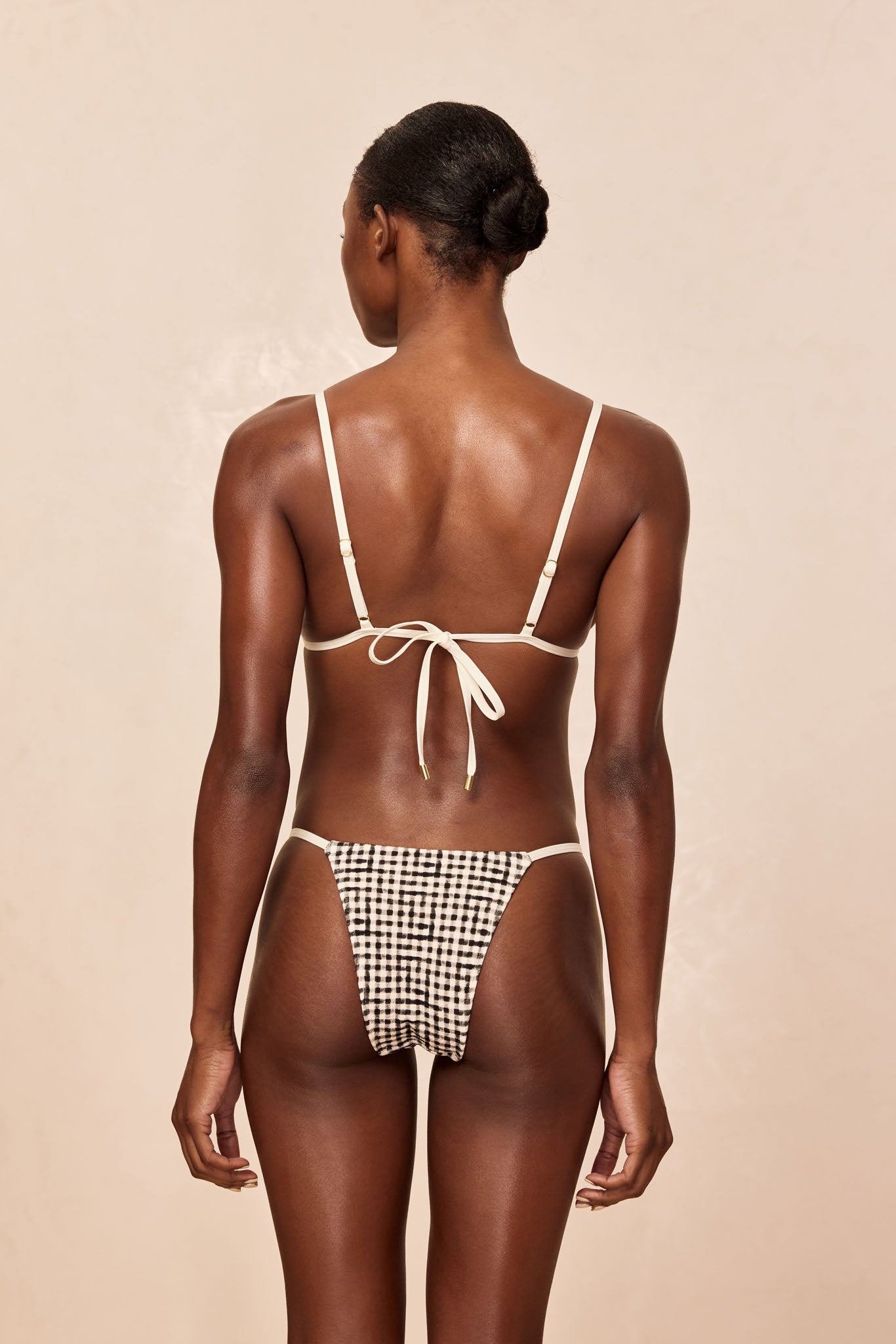 Rear view of model wearing cream-strapped bikini; checkered black-and-white high-cut bottoms with tied back bow.