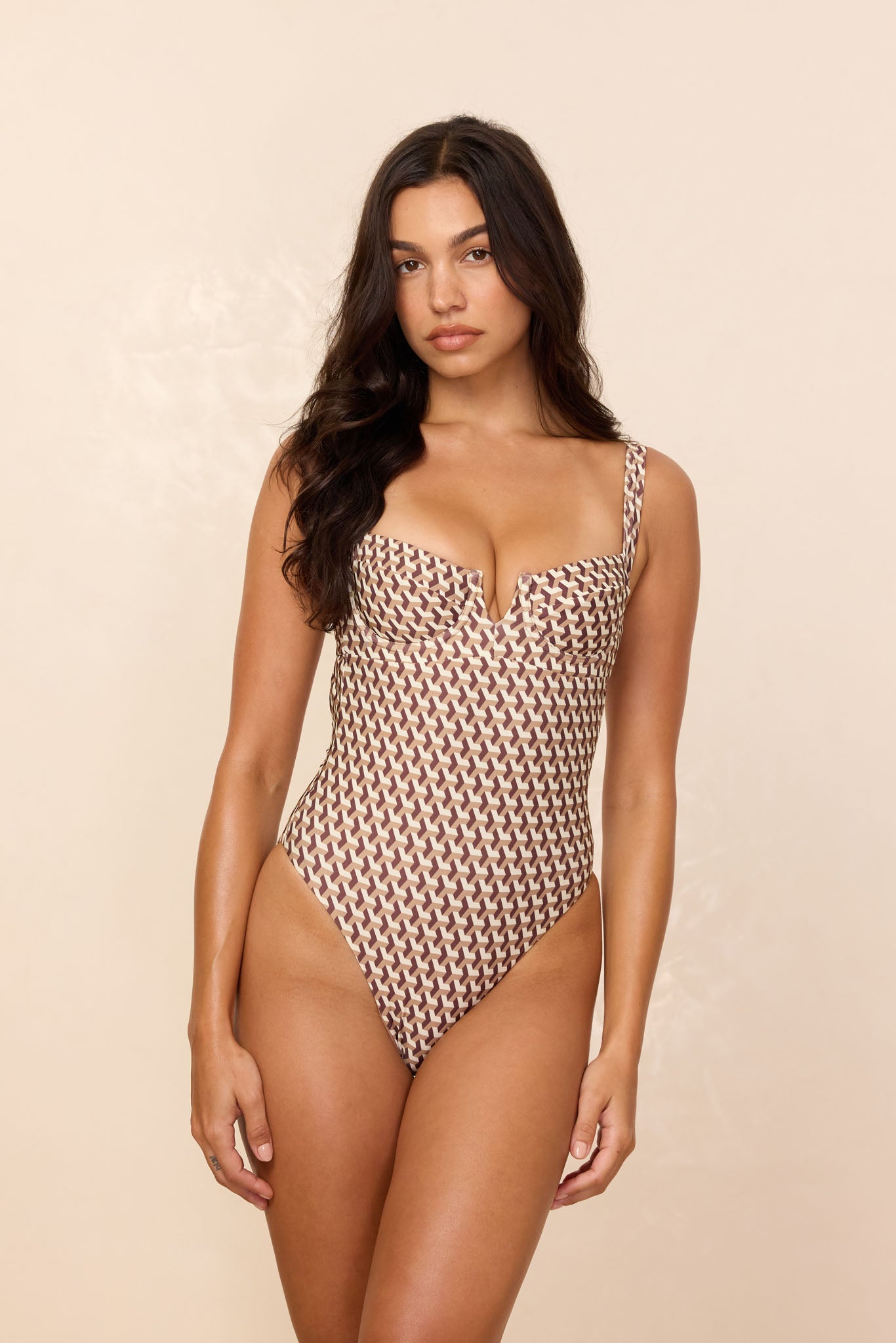 Model wearing one-piece swimsuit with brown-and-cream geometric pattern and V-shaped sweetheart neckline