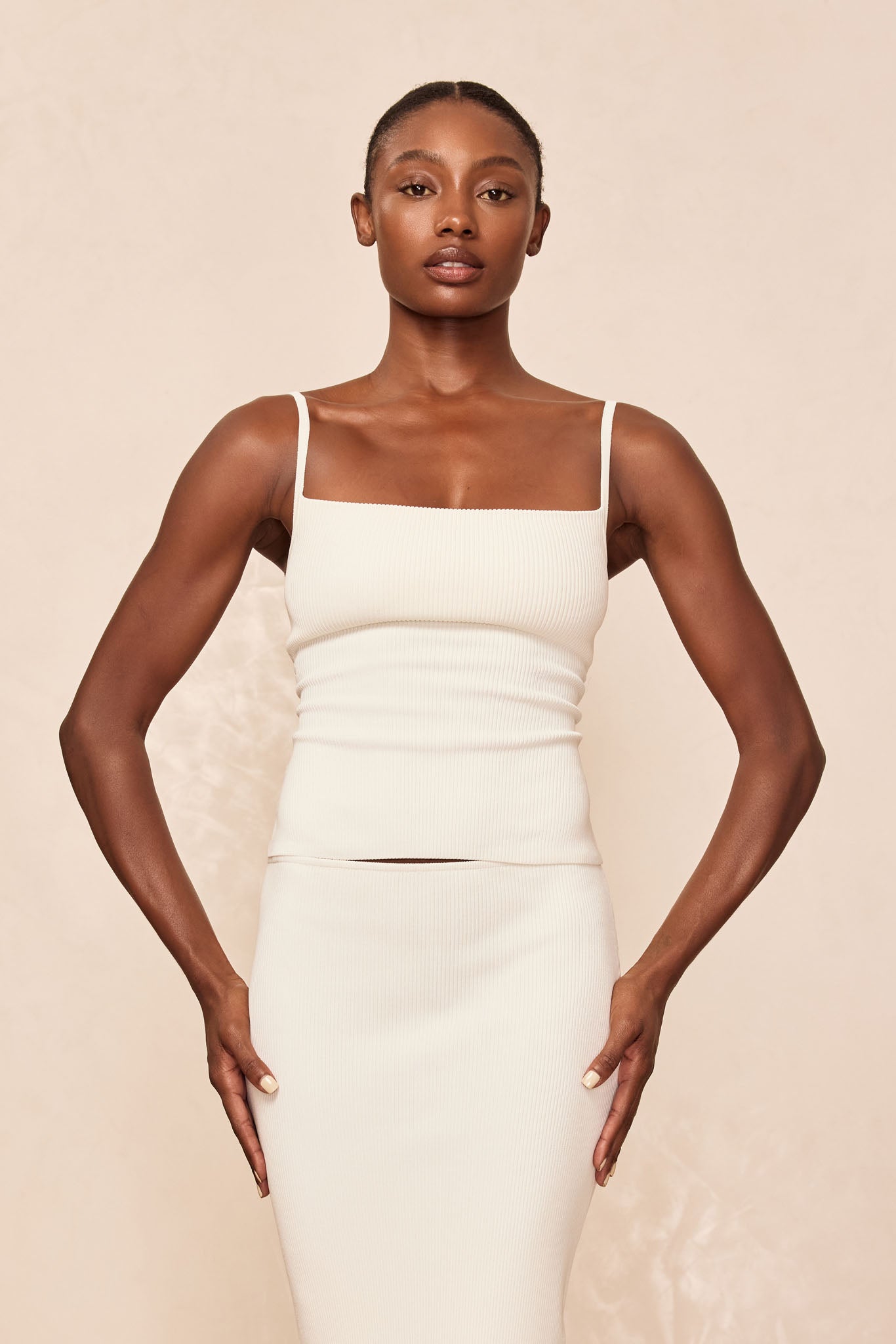 Woman wearing cream ribbed square-neck tank with thin straps and matching fitted midi skirt, hands resting at hips