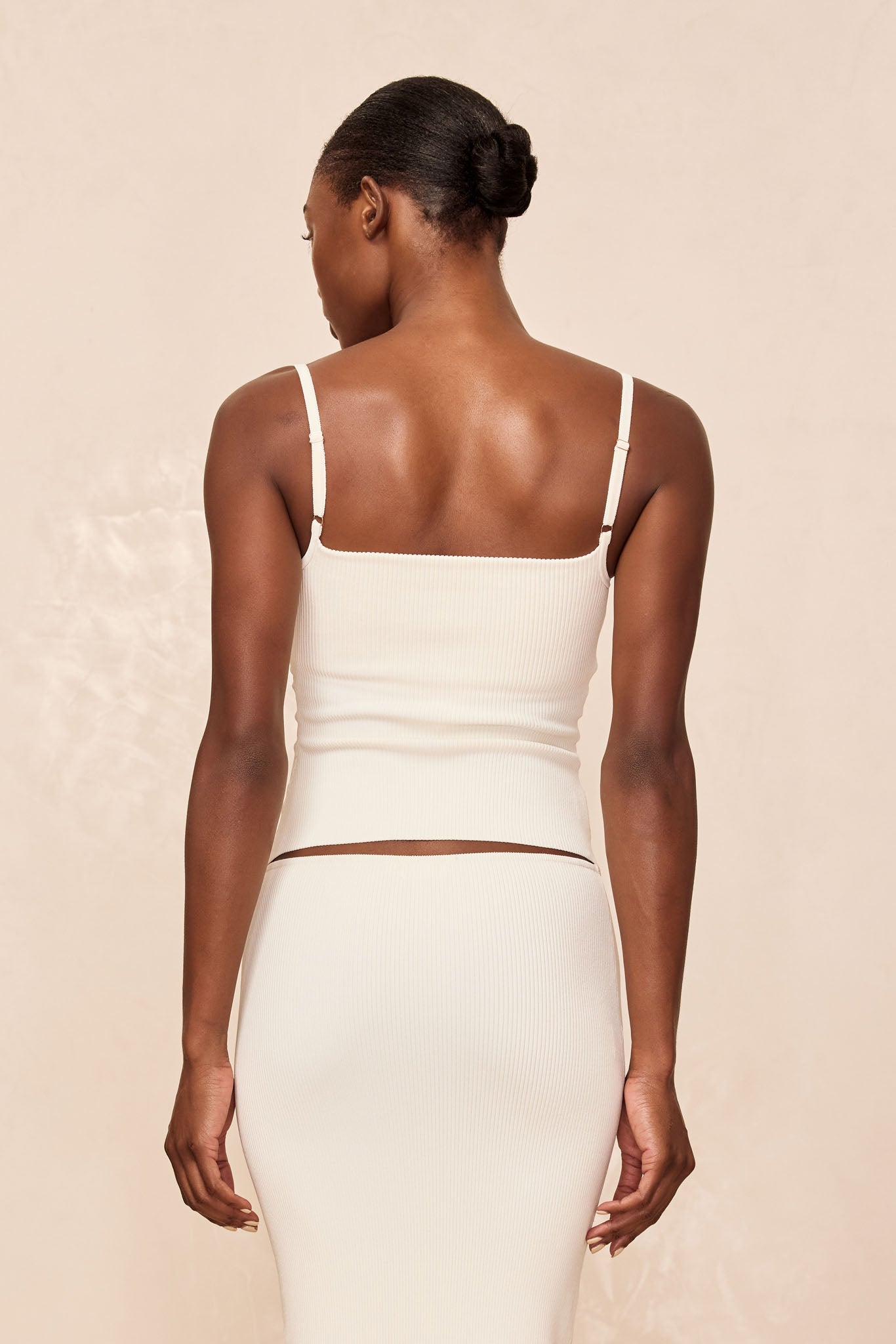 Back view of a woman wearing a cream ribbed camisole and matching skirt, hair styled in a low bun.