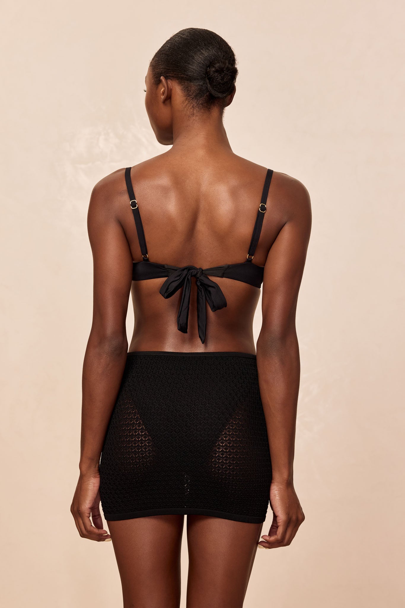 Back view of model wearing a black bikini top tied in a bow and a textured black mini slip skirt