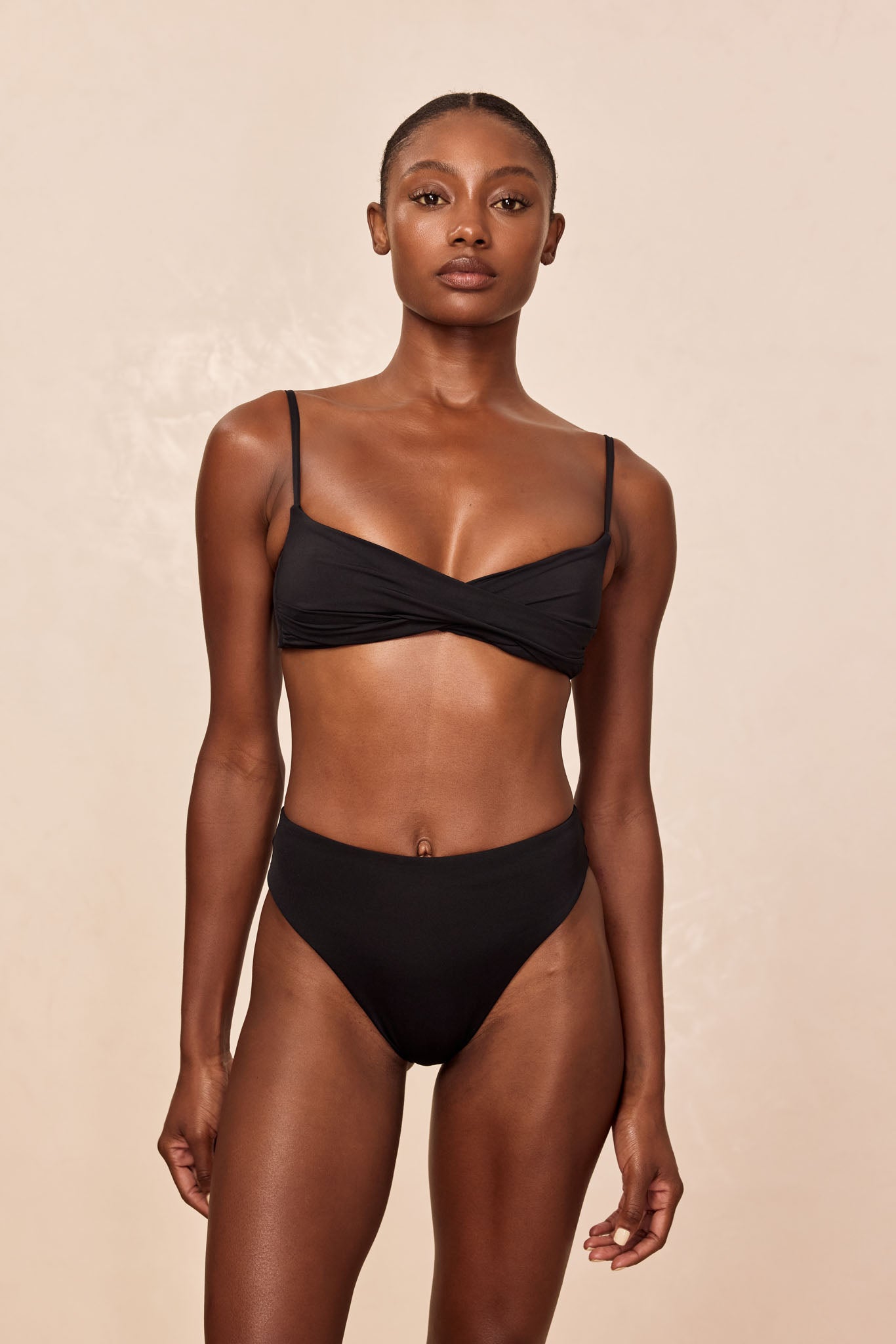 Model wearing black twist-front bikini top with thin straps and high-waist bottoms, front view on neutral background.