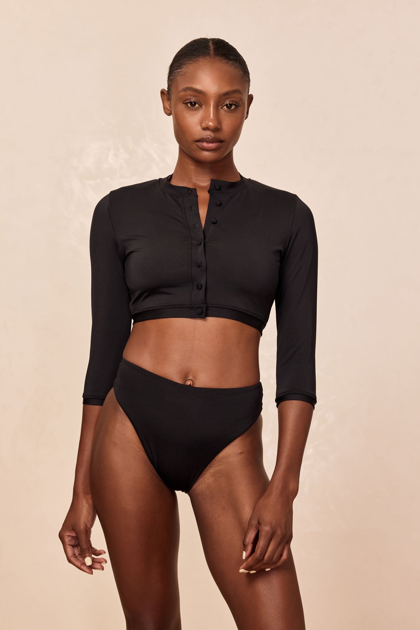 Front view of model in black cropped henley swim top with three-quarter sleeves and matching high-waist bikini bottoms.