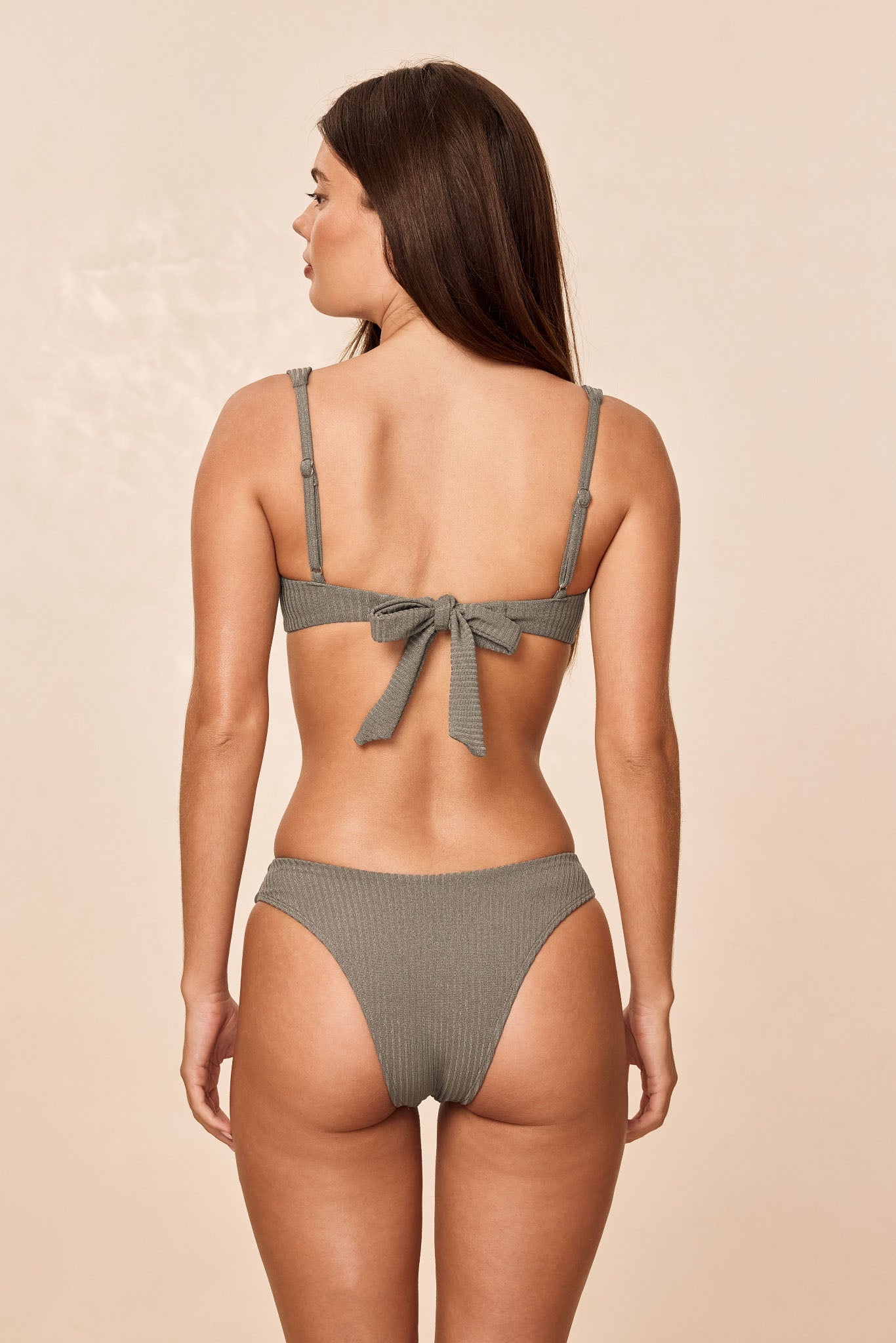 Back view of Cala Roja Top in Steel Lurex Rib showcasing adjustable straps and tied back bow on model against neutral background