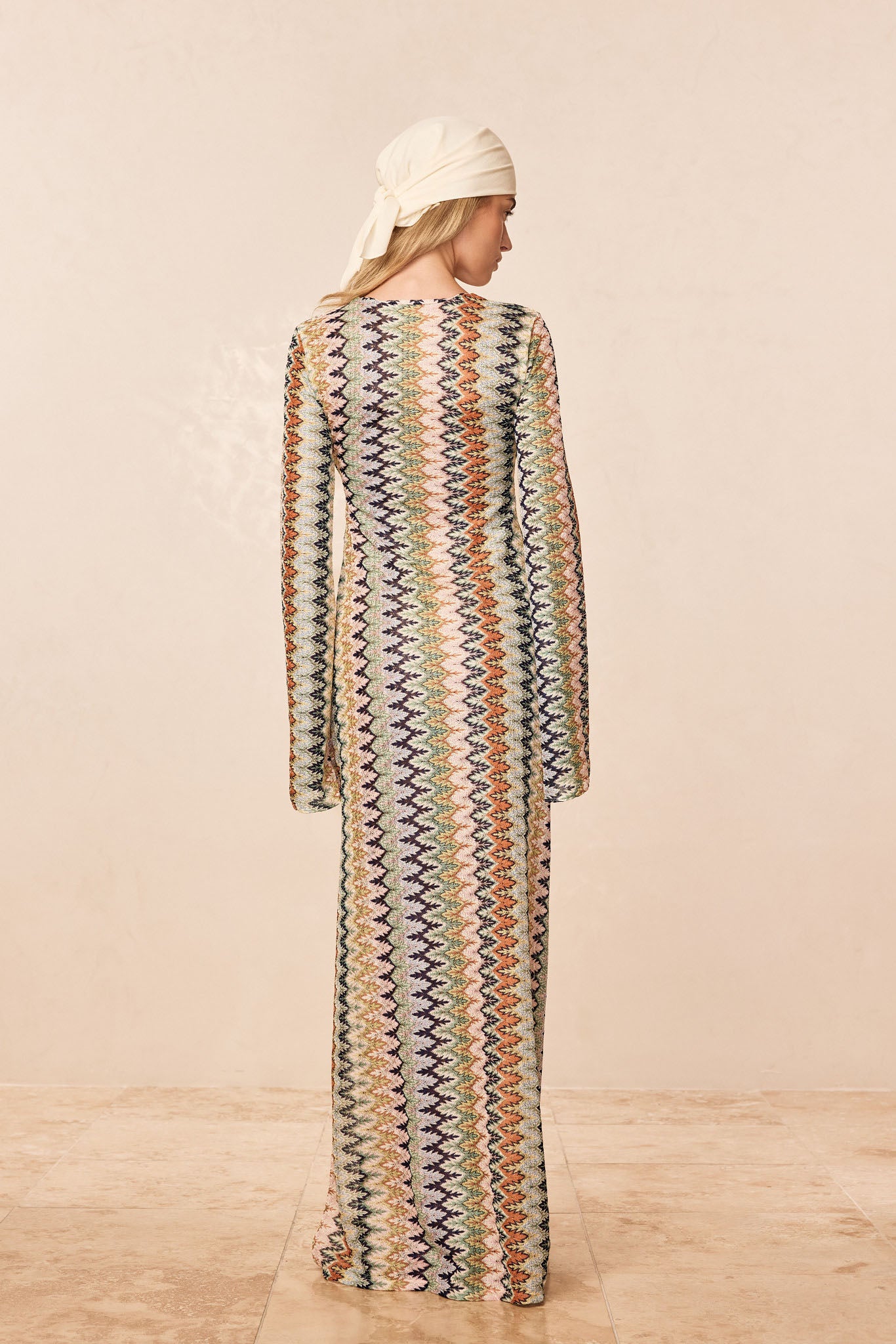 Rear view of Corossol Dress, Porto Cervo Multi, showing long sleeves and multicolored zigzag knit on a neutral background
