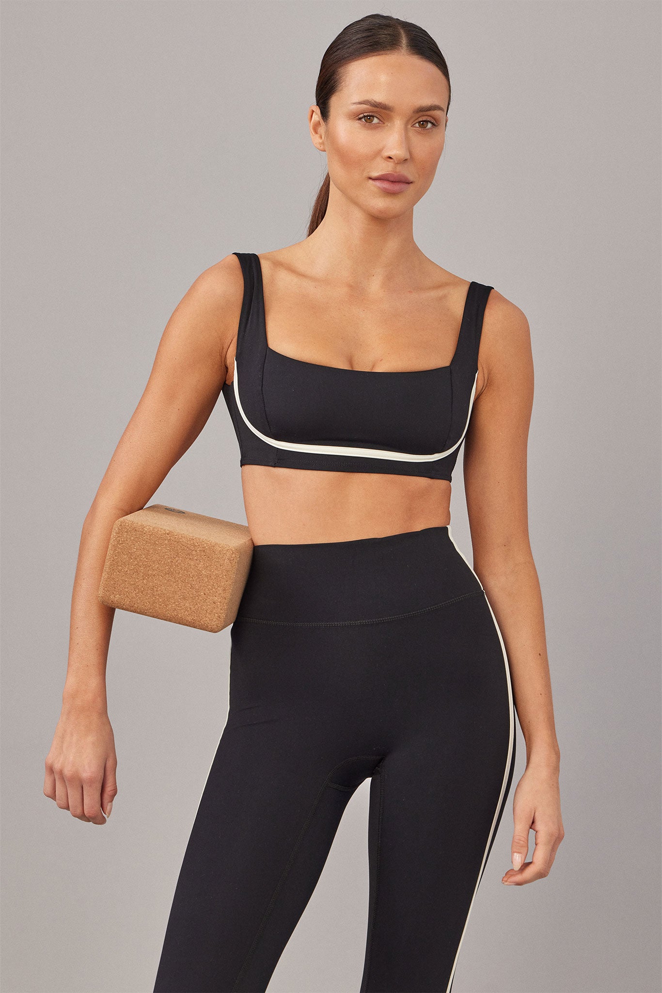 Woman in black sports bra and high-waist leggings holding a cork yoga block under her arm.