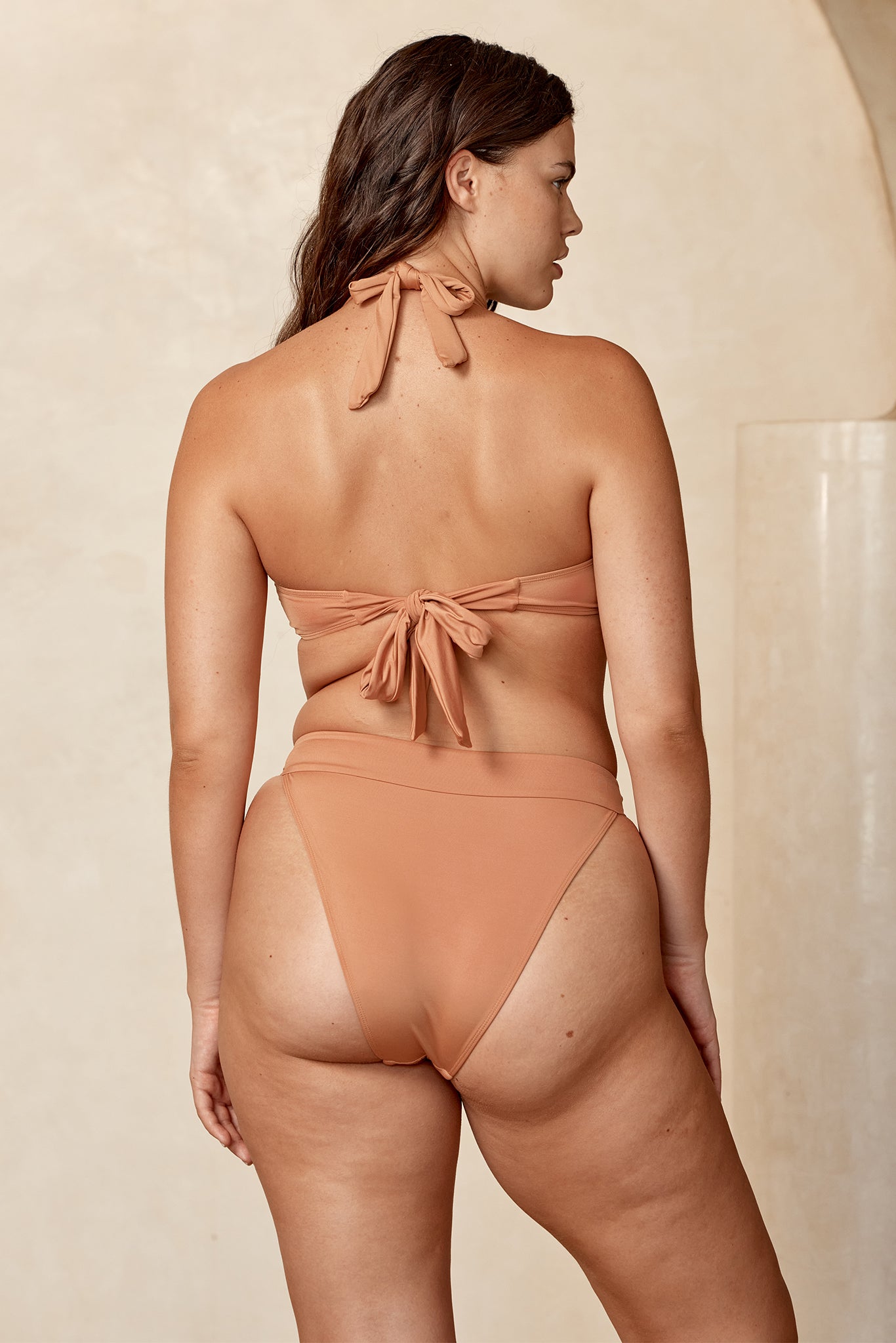 Back view of model wearing tan tie-back bandeau top and high‑waist bikini bottoms.