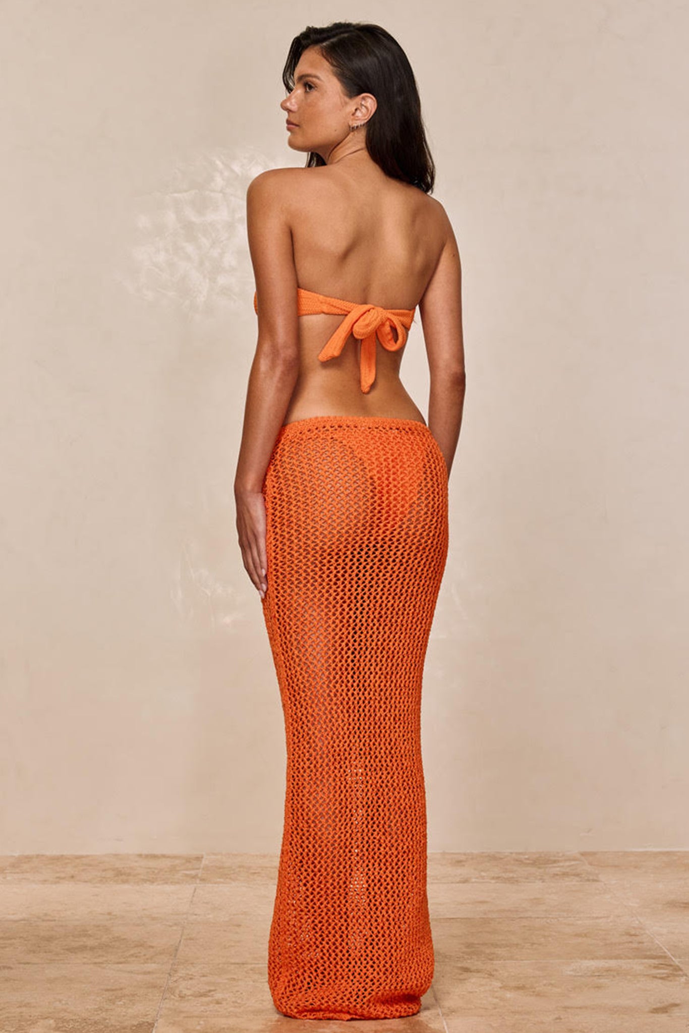 Woman turned away wearing orange knit crochet maxi skirt with matching bandeau bikini tied at back