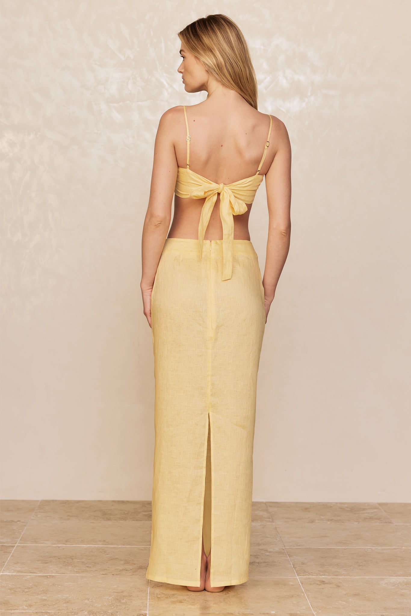 Back view of model wearing yellow tie-back crop top and matching high-waist maxi skirt with center back slit.