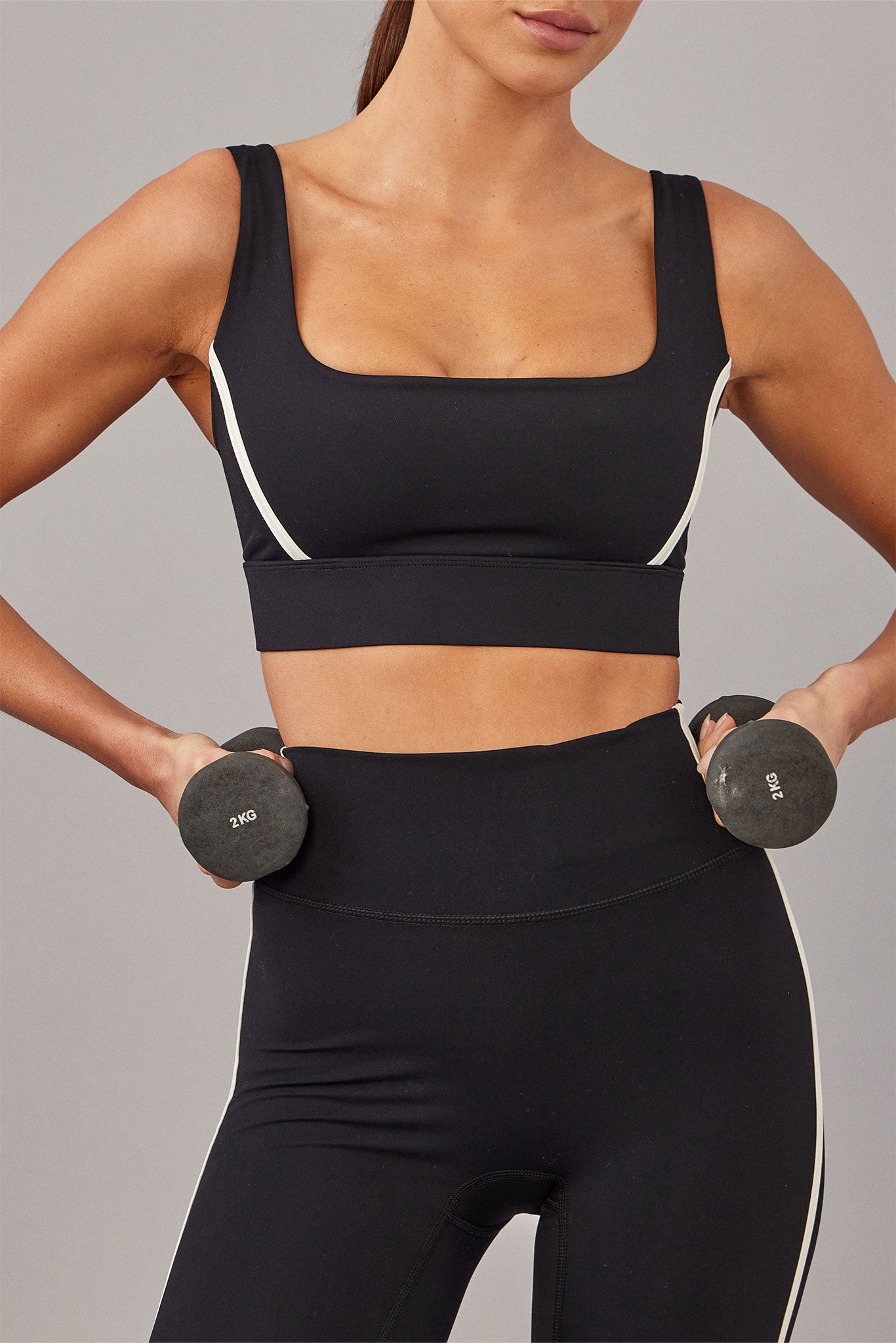 Woman in black square-neck sports bra and high-waist leggings holding 2KG dumbbells at her hips