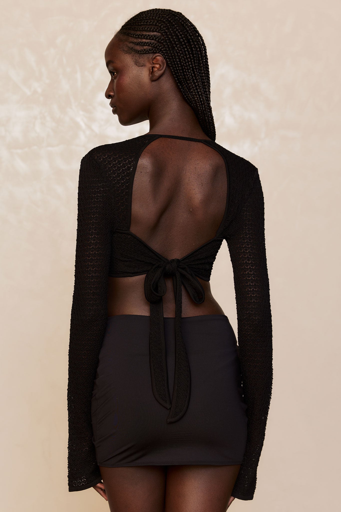 Rear view of woman with braided hair wearing black open-back knit tie-top and fitted black mini skirt.
