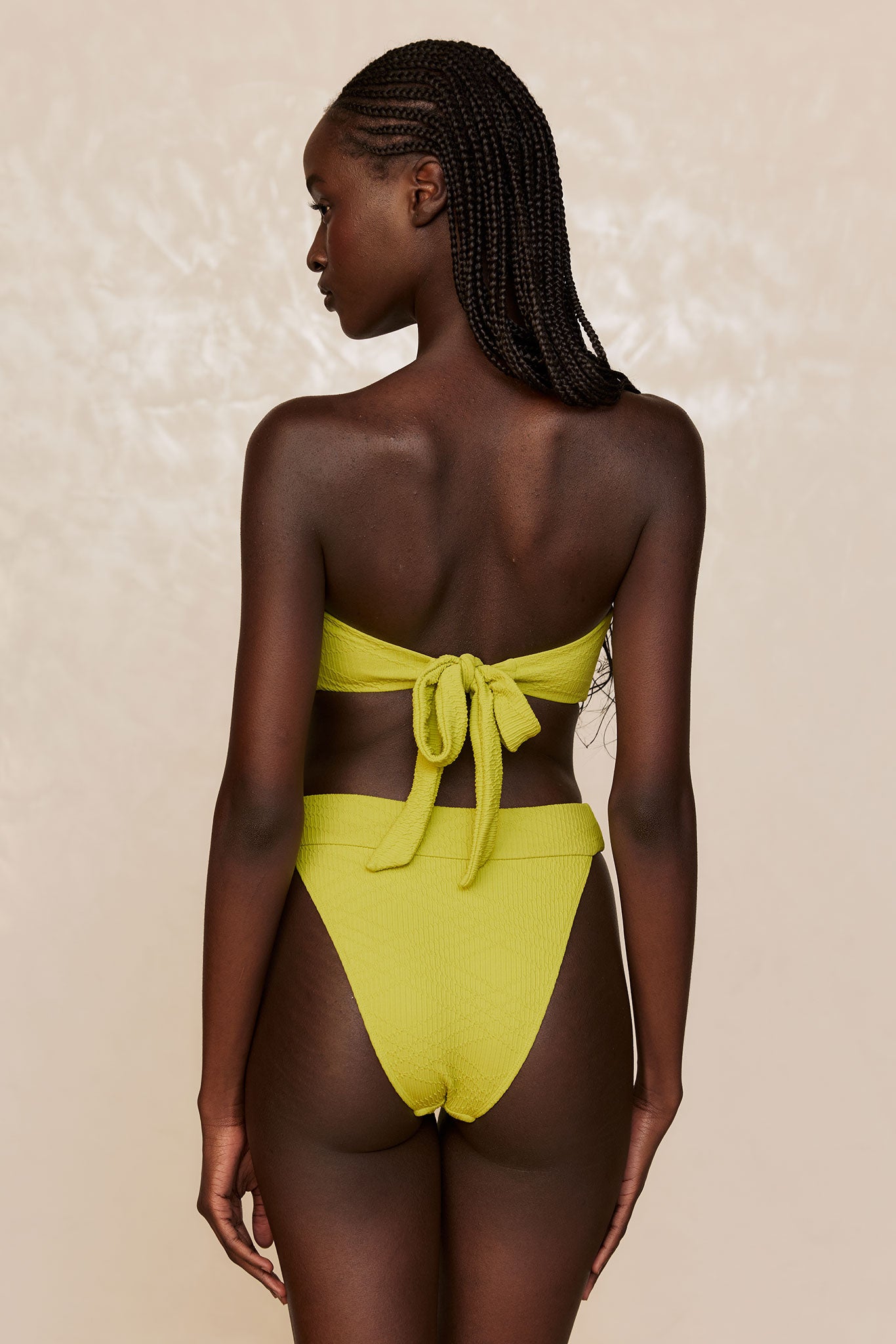 Rear view of woman with braided hair wearing lime-green textured tie-back bandeau bikini and high-waist bottoms.