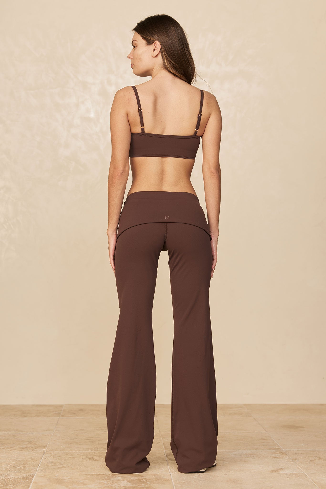 Woman shown from back wearing brown crop bra and high-waist flared pants; small M logo on the center back waistband.