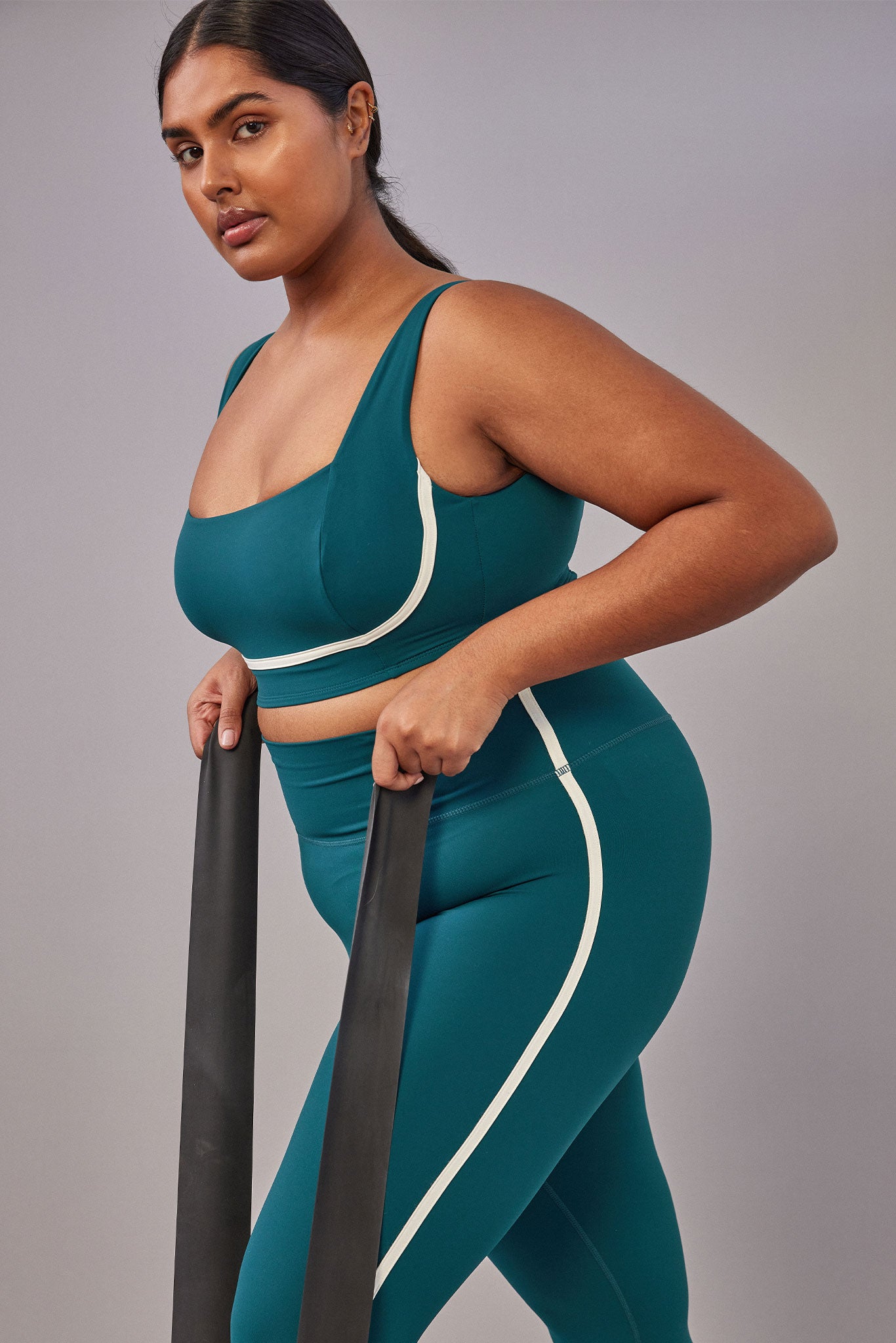 Plus-size woman wearing teal sports bra and high-waist leggings using two resistance bands, side view