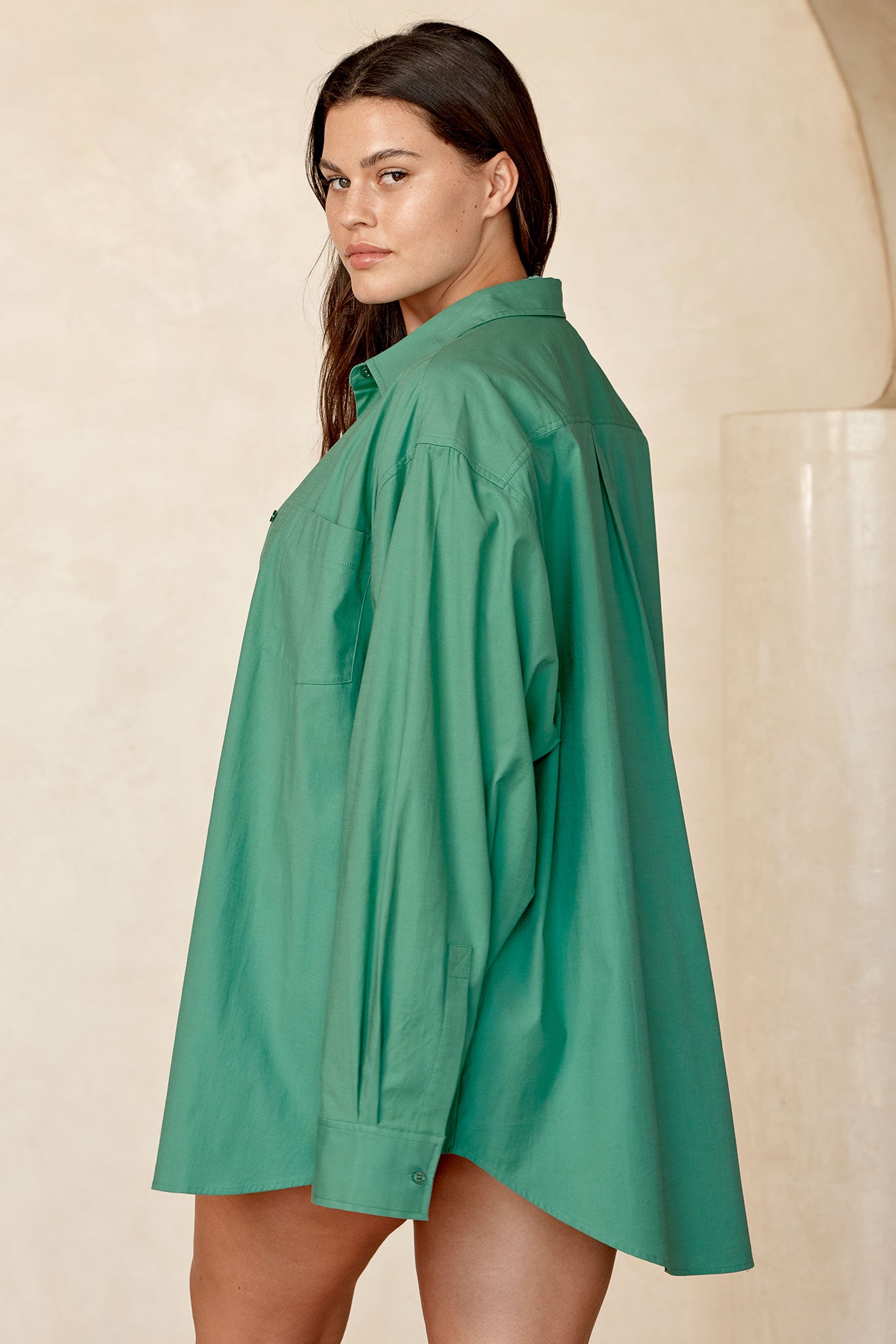 Plus-size model in oversized green button-front shirt, side view looking over her shoulder.