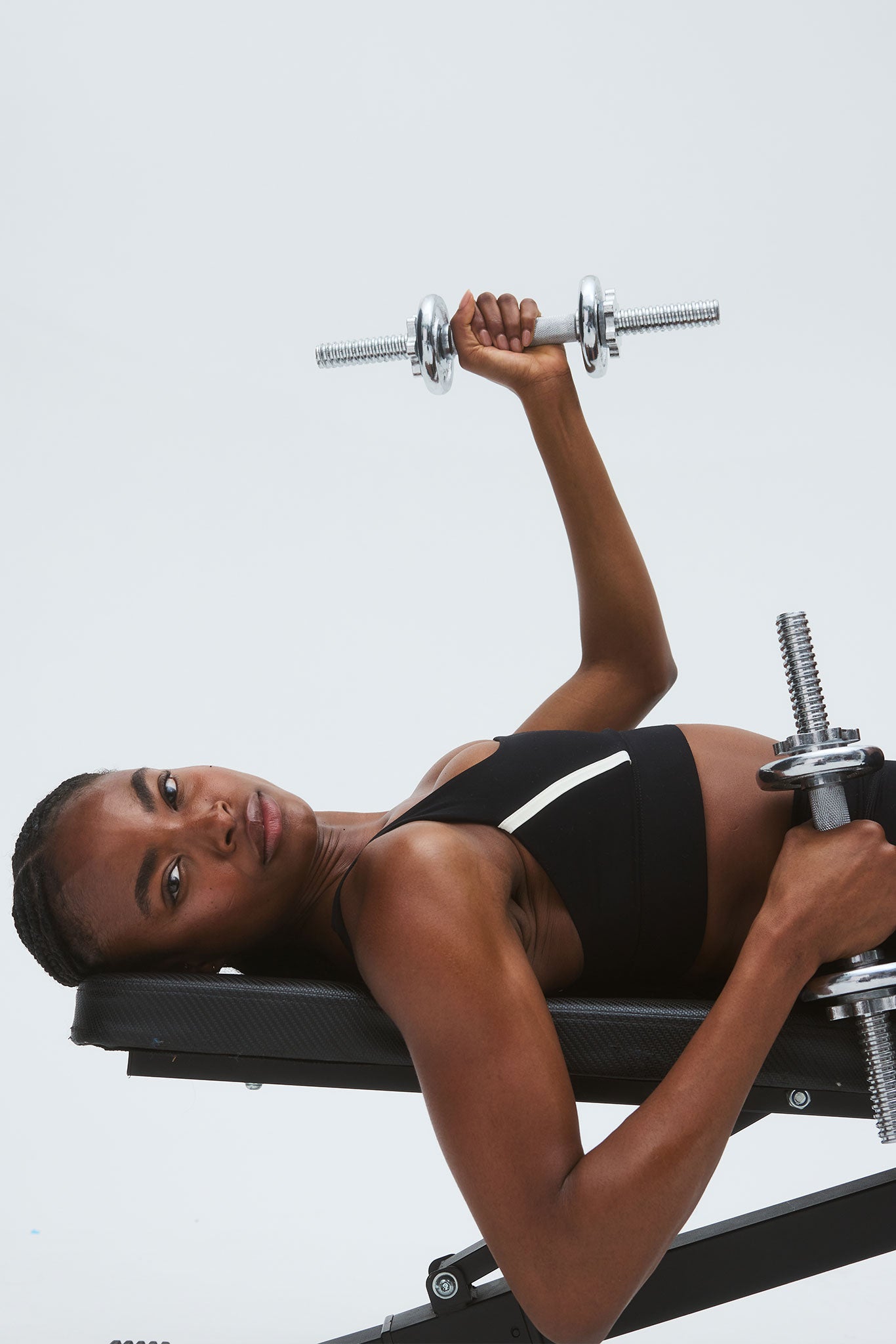 Person lying on a bench performing a dumbbell chest press, holding one dumbbell overhead and another near their torso.