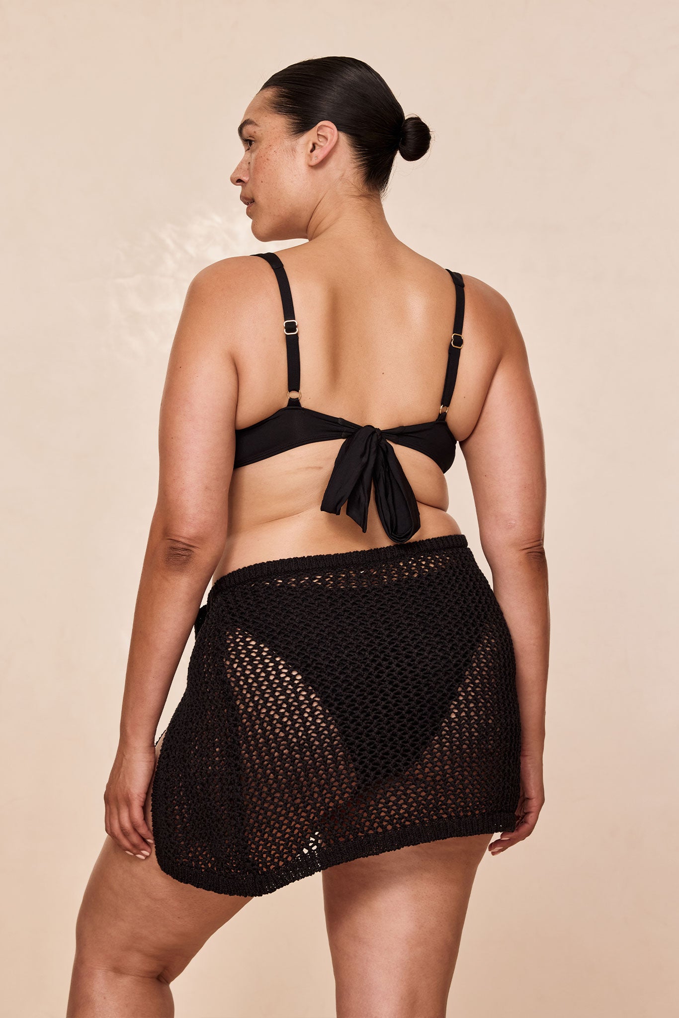 Rear view of woman modeling a black tie-back bikini top and a black crocheted mesh skirt cover-up