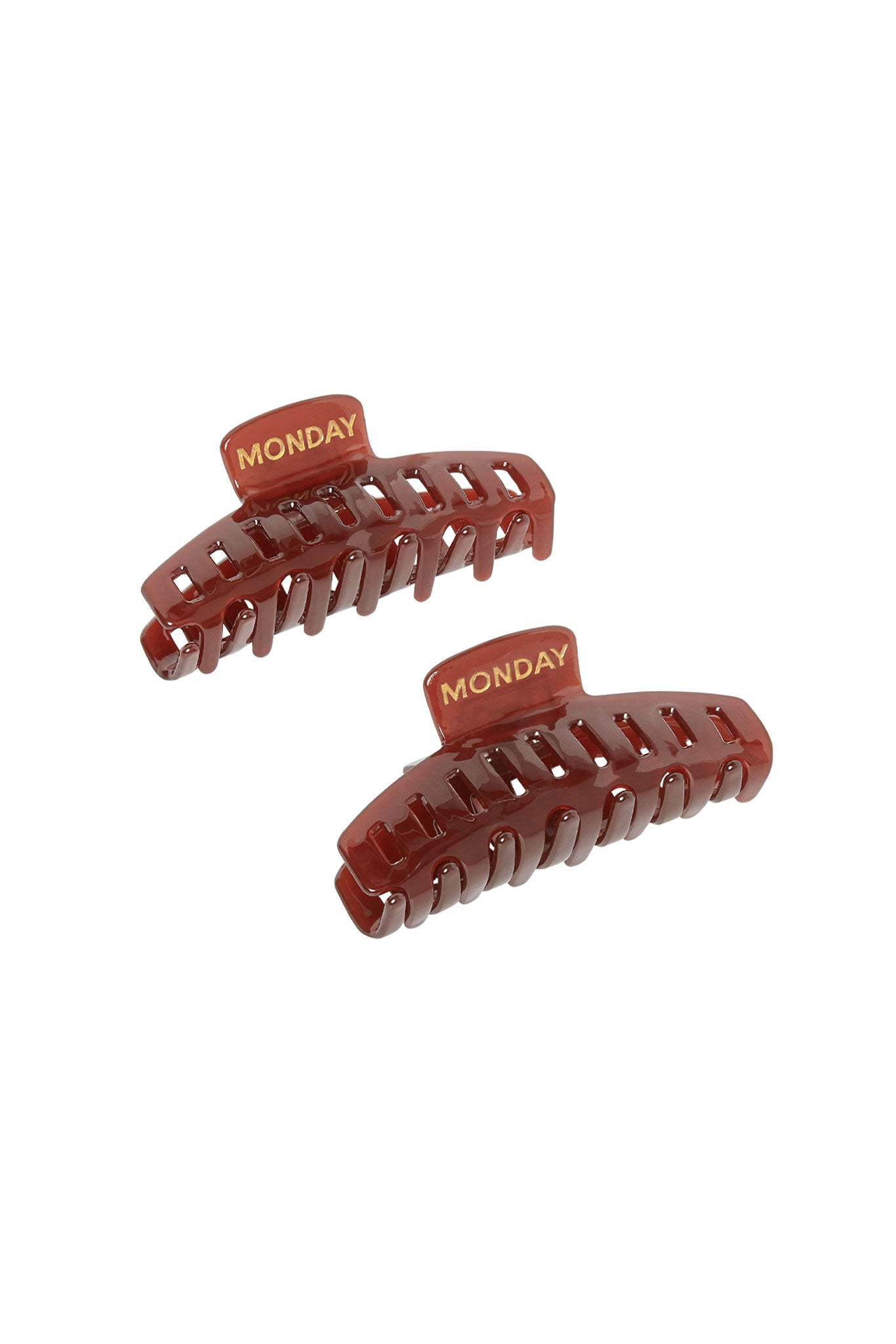 Two brown hair claw clips with gold MONDAY text on their top tabs